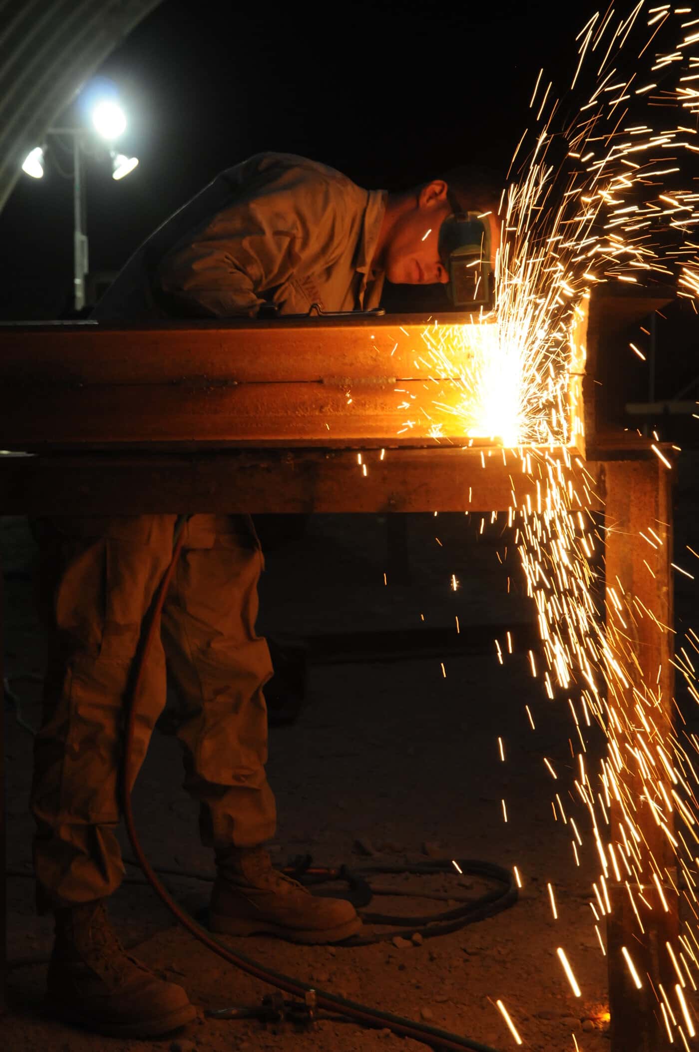 A welder working over structural steel under industrial light.